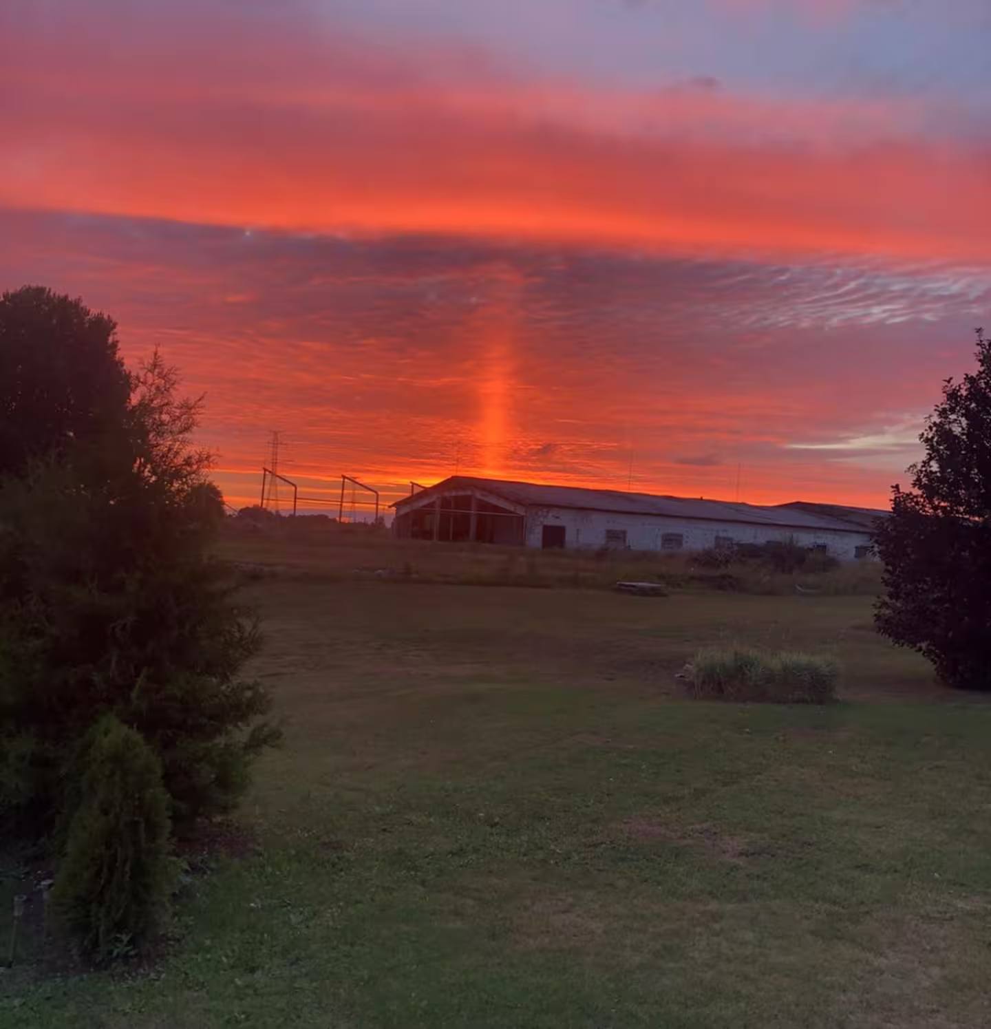 Kräftig rot gefärbter Abendhimmel über dem Hof, im Vordergrund Rasen, Bäume und ein Gebäude am Horizont.