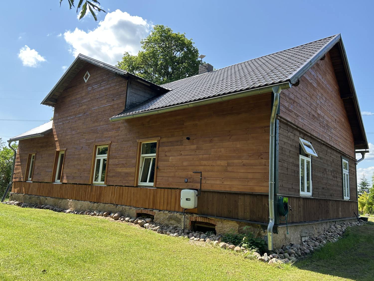 Giebelseite des Holzhauses mit höherem Aufbau und Rautenornament im Giebel, Feldsteinsockel und weiß gefassten Fenstern.