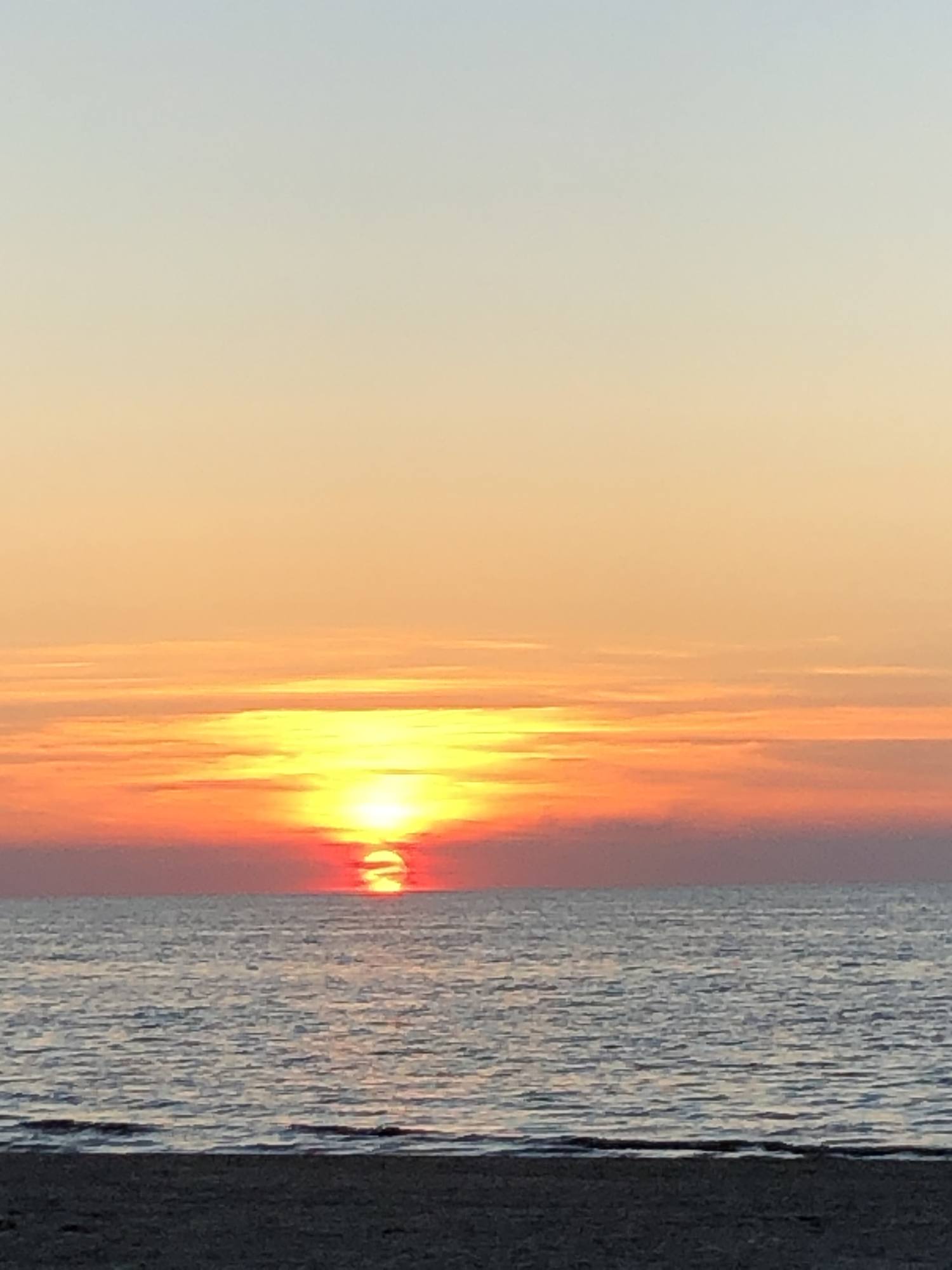 Abendsonne hinter einem Wolkenband über dem offenen Meer, der Himmel in Orange- und Blautönen.