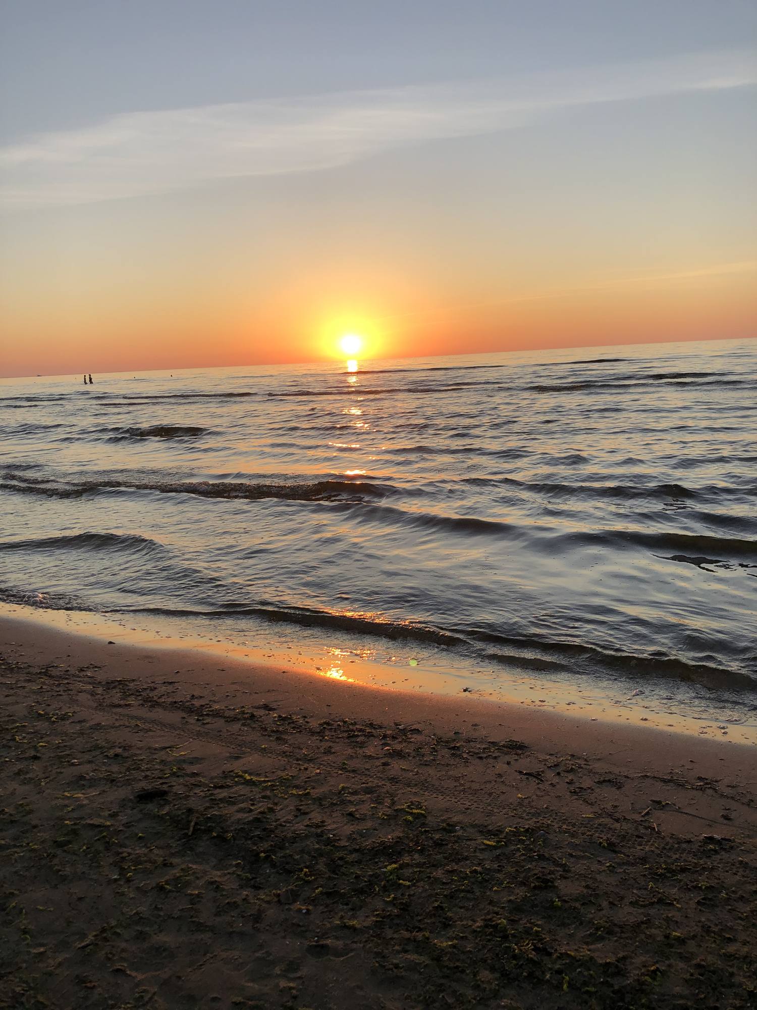 Sonnenuntergang über der Ostsee, die Sonne steht dicht über dem Wasser, im Vordergrund auslaufende Wellen auf dem Sand.