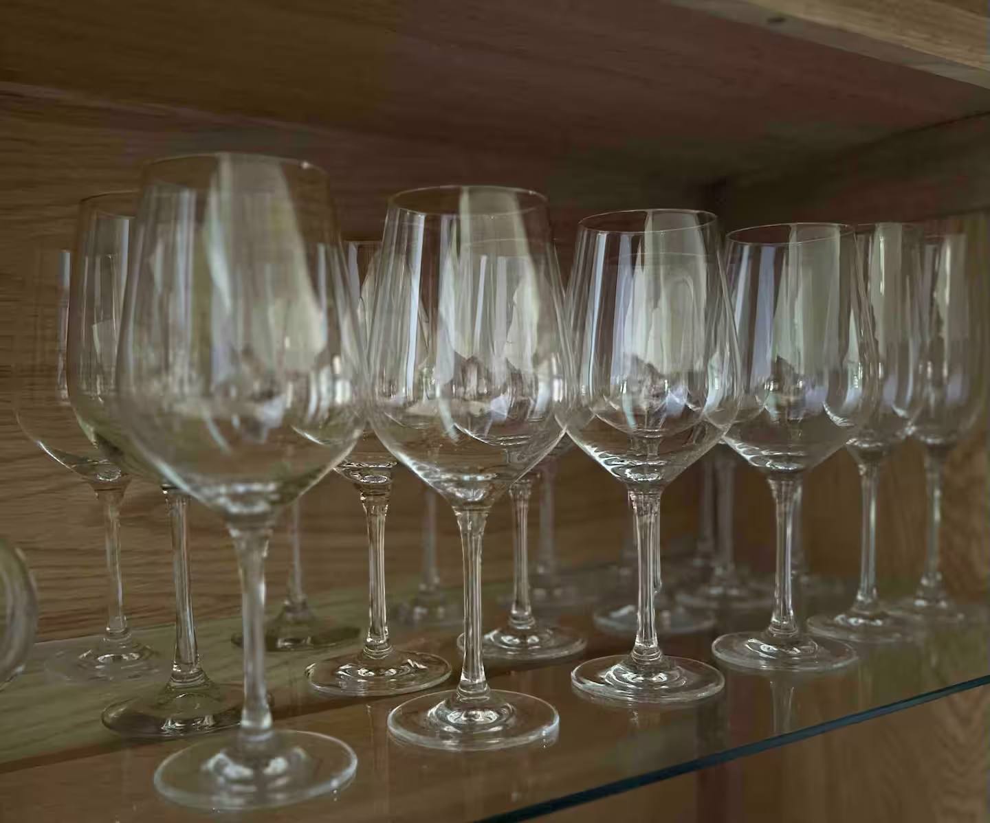 Reihe von Weingläsern und Sektgläsern auf einem Glaseinlegeboden in einem Holzschrank.